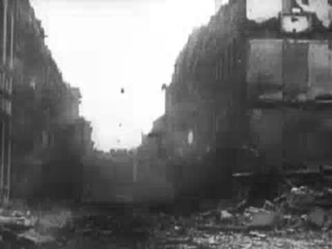 Damaged buildings flanking a dusty, debris-filled street corner after an attack, WWII