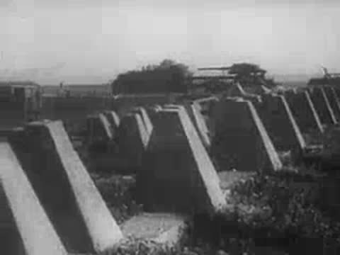 Concrete anti-tank teeth barriers lined up in a field with military vehicles, WWII