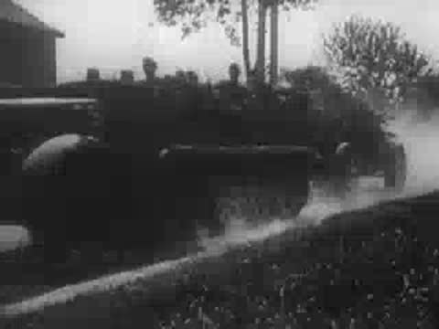 Military personnel with heavy artillery and trucks moving along a dusty road, WWII