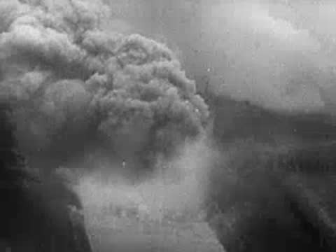 Large explosion with thick grey smoke billowing over a landscape.