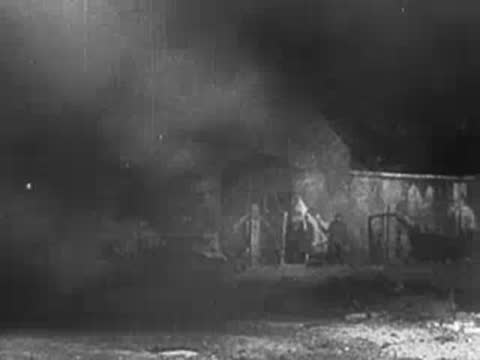 Soldier walking past burning wreckage and buildings in a destroyed street.