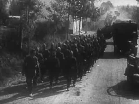 Column of troops marching down a road flanked by military trucks.