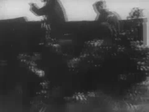 Soldier riding on the back of a moving military truck, period footage.