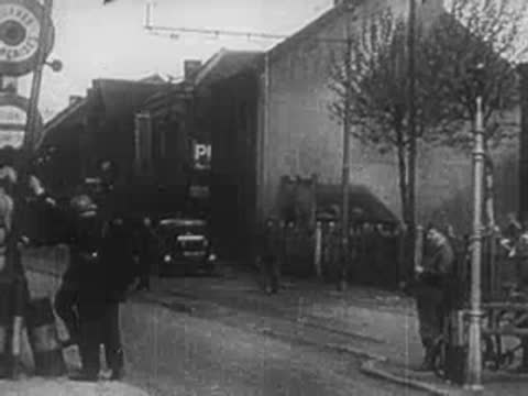 Troops in helmets boarding trucks parked along a town street.