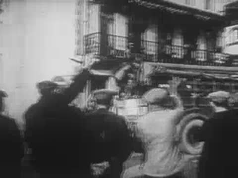 Civilians waving at a passing convoy from a roadside balcony.