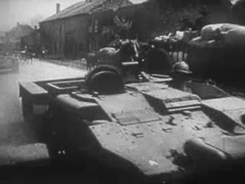 Tracked military transport vehicles parked near rural buildings and carts.