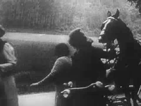 Refugee women and children walking alongside horse-drawn carts on a road.