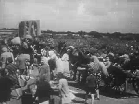 refugees walking with carts and belongings across fields during wartime