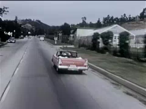 Red convertible driving away down a straight suburban street.