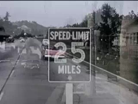 Red convertible driving past a street sign reading Speed Limit 25 Miles.