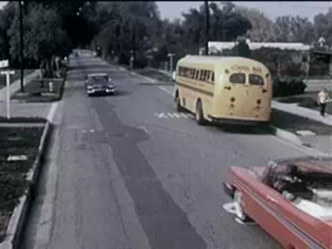 Red convertible driving past a parked yellow school bus on a suburban street.