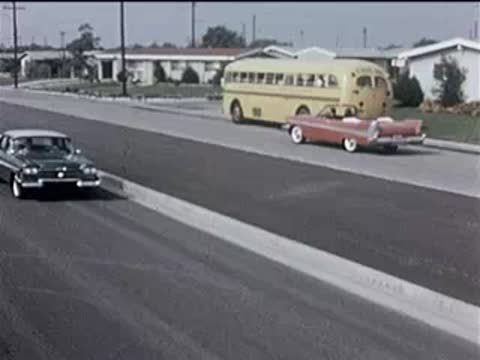 Side view of a red convertible driving past a parked yellow school bus.