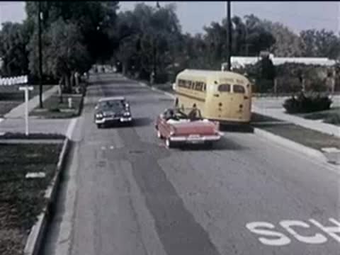 Overhead view of a red convertible driving on a suburban street near a bus.