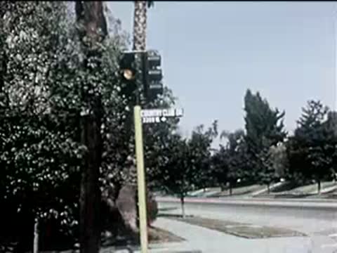 traffic light turns green and cars drive forward down a suburban street, 1950s