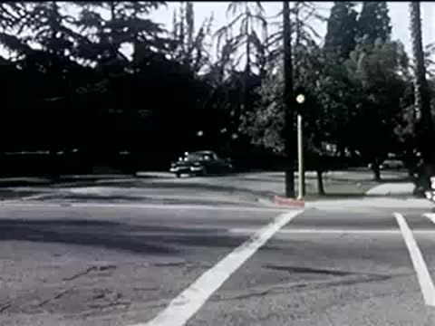 red convertible driving across an intersection on a sunny day, 1950s