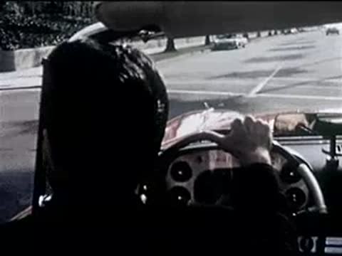 driver in a red convertible driving through a suburban intersection, 1950s