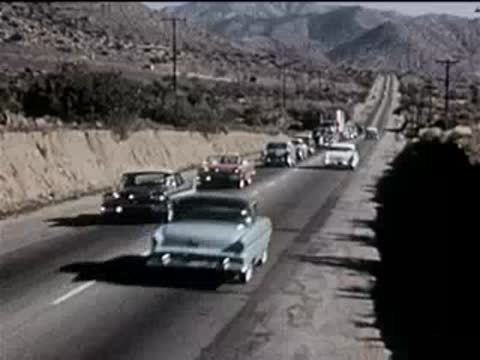 traffic driving slowly on a multi-lane highway near arid hills, 1950s