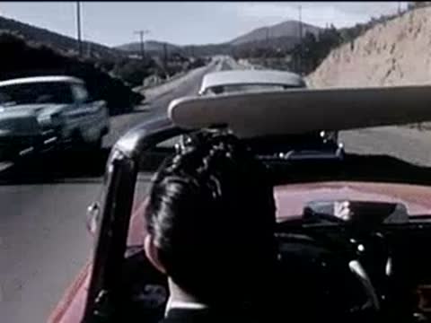 driver in a convertible following traffic on a sunny highway, 1950s