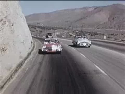 red convertible driving on a winding highway past rocky hills, 1950s