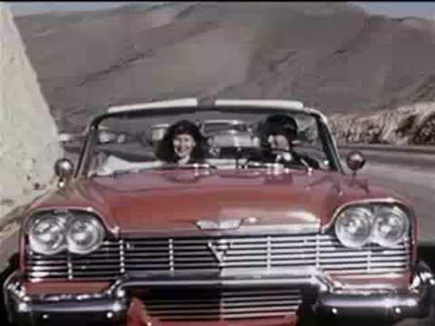 front view of a red convertible driving on a sunny highway, 1950s