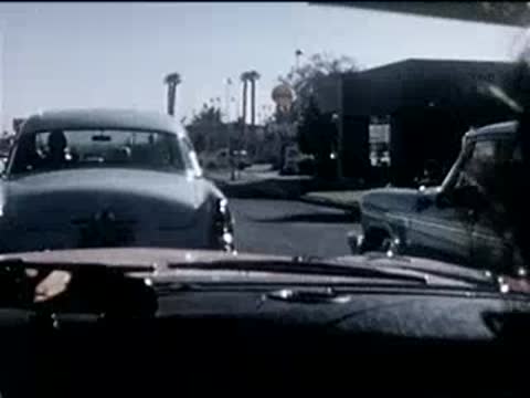 view from inside a car following other vehicles down a street, 1950s