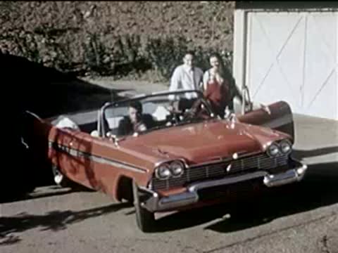 Red convertible car parked in a driveway with two people standing near it.