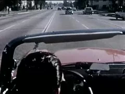 driver in a convertible driving along a busy highway with traffic, 1950s