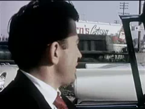 side profile of a man driving a convertible along a city street, 1950s
