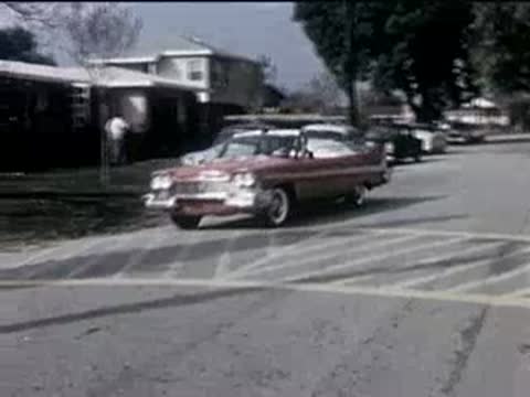 red convertible driving through a suburban intersection on a sunny day, 1950s