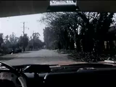 view from inside a car driving down a quiet tree-lined suburban street, 1950s