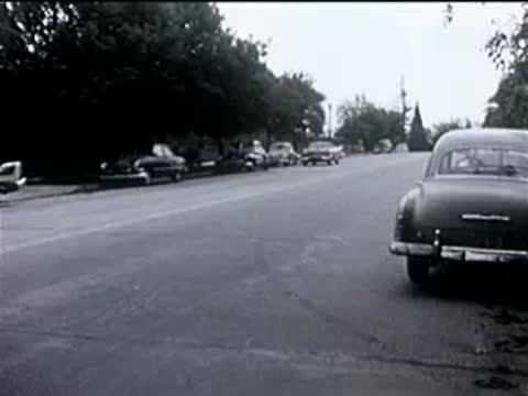 view from inside a car driving past a cyclist on a suburban street, 1950s
