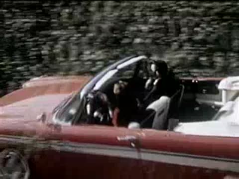 Red convertible driving on a suburban street being pulled over by police officer.