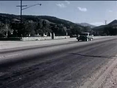A green vintage sedan driving along a road through a valley landscape.