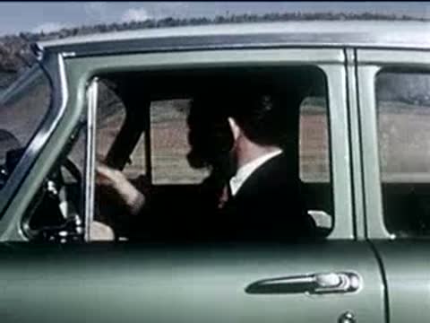 Side view of a man driving a green vintage car, gesturing angrily.