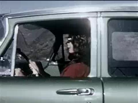 Side view of a woman driving a green vintage car on a road.