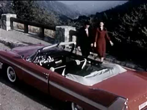 A red convertible parked on the side of a road near a stone wall.