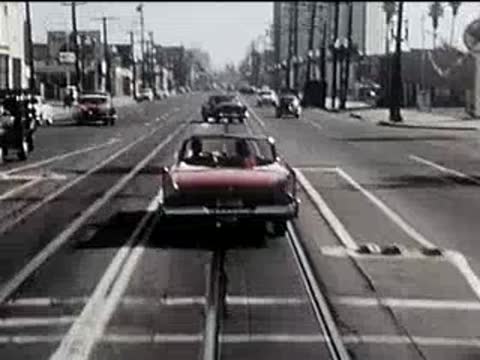 Rear view of a red convertible driving down a city street with tram tracks.