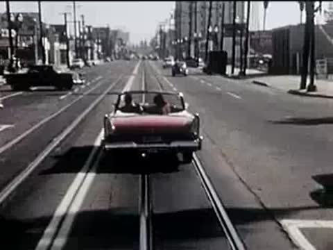 Rear view of a red convertible driving away down a multi-lane city street.