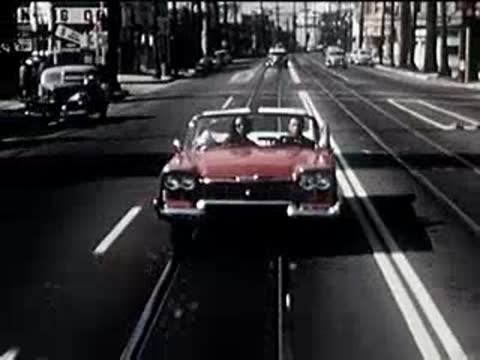 Front view of a red convertible driving towards the camera on a city street.