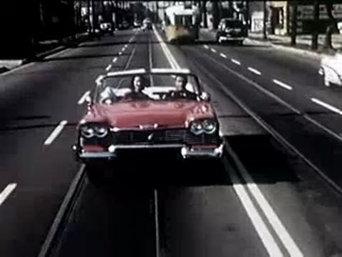 Front view of a red convertible driving along a city street with tram tracks.