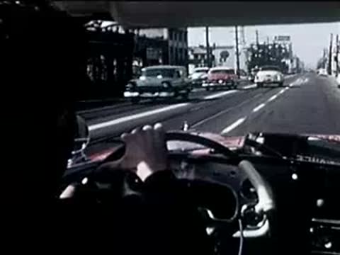 Rear view of a red convertible driving down a city street with traffic.