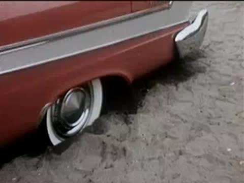 Close-up of the rear wheel of a red car parked on sandy ground.