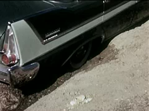 Close-up of a green car's rear wheel spinning and kicking up dust.