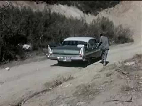 A person changing a flat tire on a green car parked on a roadside.