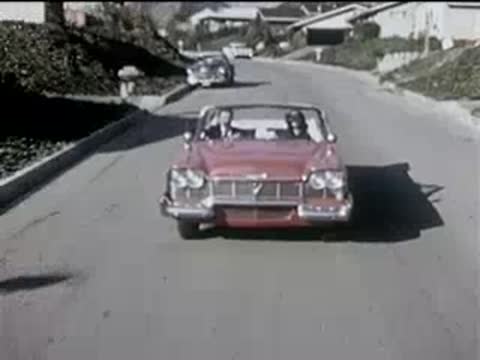 Red convertible driving forward down a suburban residential street.