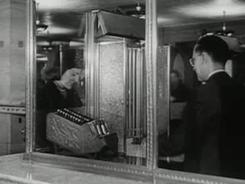 Bank teller working behind the glass window with an adding machine.