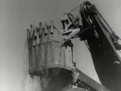 An excavator arm lifts a large bucket full of excavated earth.