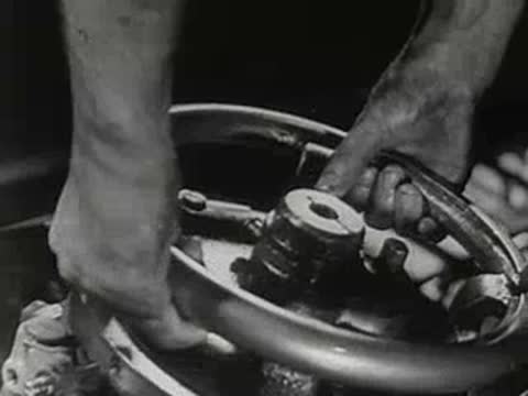 Close-up of hands turning a heavy metal wheel on machinery.