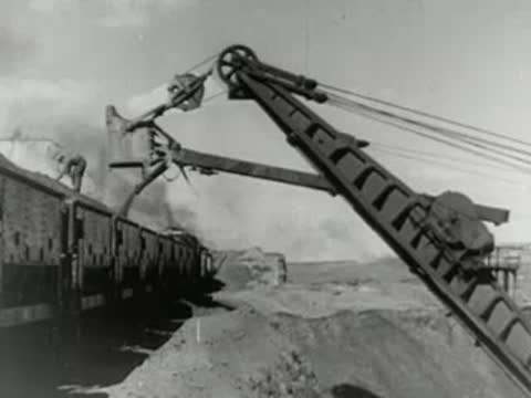 An excavator empties earth into a long line of freight cars.