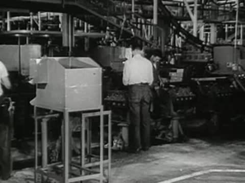 Workers in an industrial factory assembling parts near metal equipment.